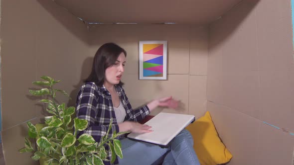 Concept Idea of a Little Roomdisgruntled Young Woman in a Small Cardboard Box with a Laptop alt