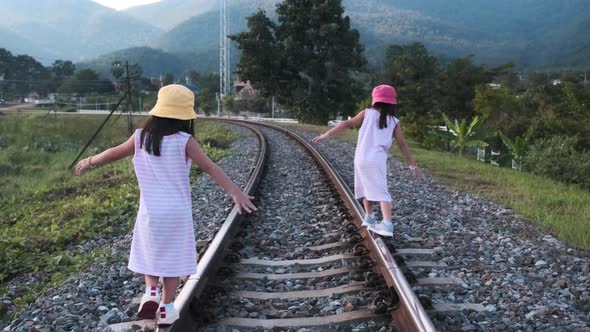 Two cute Asian girls balancing on the railroad tracks with their arms outstretched. alt