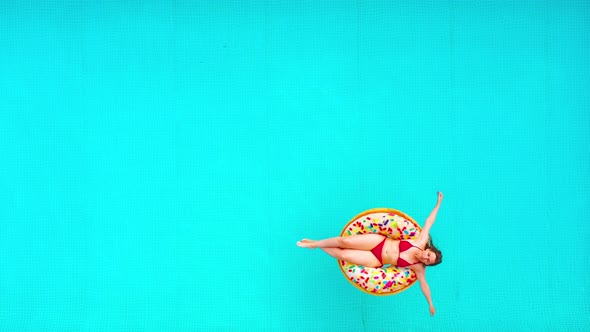 Aerial View of a Woman in Red Bikini Swimming on a Donut in the Pool alt