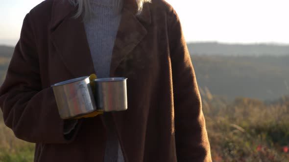 woman hold mugs of tea in mountains Sudetes in November in sunset