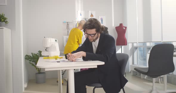 Three Professional Fashion Designers Working in Modern Atelier alt
