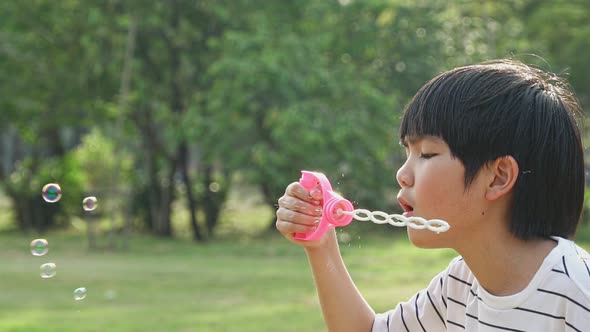 Asian boy blowing soap bubble in park