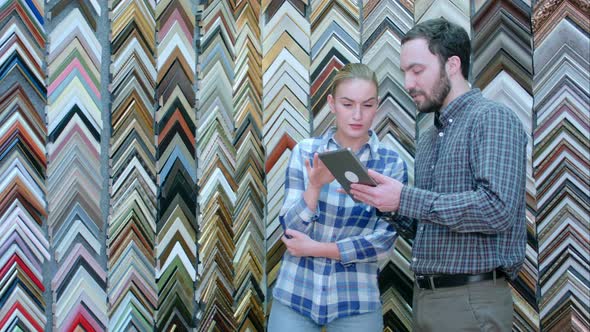 Joyful Young Woman Worker Talking with Customer About Picture Frame Details alt