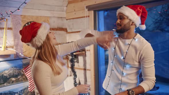 Happy Young Couple Dancing with Christmas Lights and Santa Hats alt