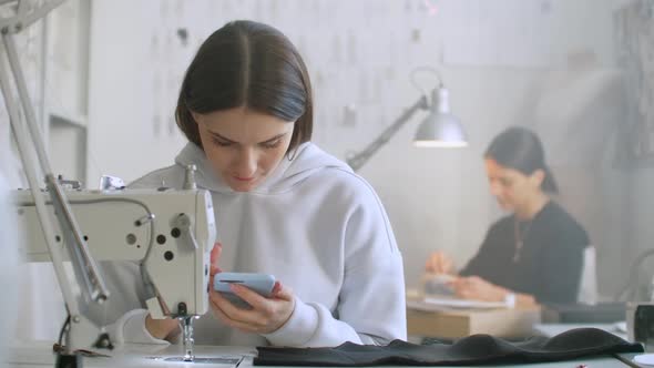 Woman Seamstress Looks at the Smartphone Screen in the Workplace alt