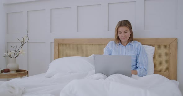 Happy Woman with Laptop Lying in Bed and Smiling. Girl in a Man's Shirt Working on a Laptop in the alt
