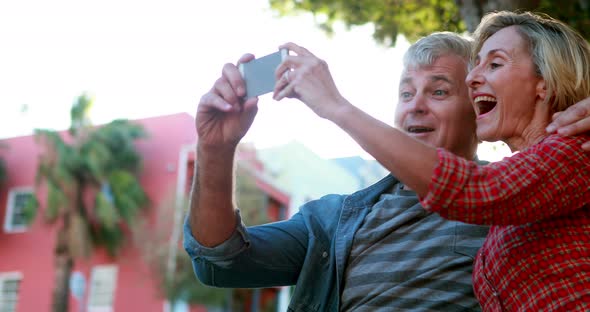 Happy Couple Sitting on Bench Taking a Selfie alt