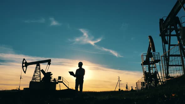 Oil Worker Walking Across an Oilfield with His Laptop. Oil Industry, Crude Oil Prices Concept. alt