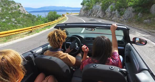Friends having fun driving on the road along the coast in red convertible alt