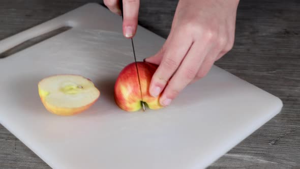 A young woman in a kitchen cutting up a red apple on a plastic chopping board alt