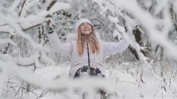 Portrait of a Teenage Girl Sitting in a Snowy Fairy Forest and Throwing Snow alt