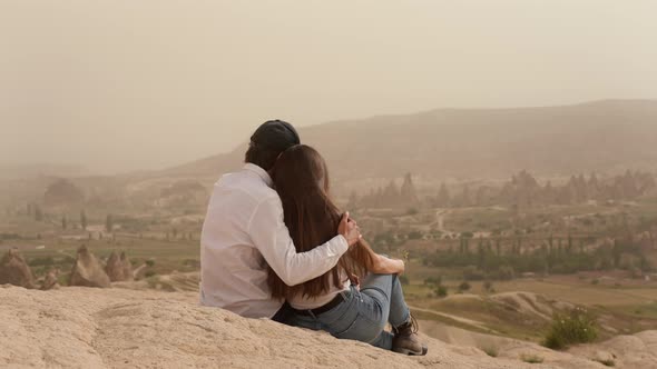Couple of Man and Woman Sit and Hug on Mountain Slope Above Valley