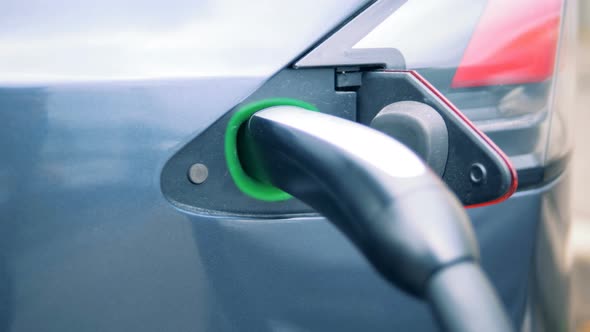 Filler Socket of an Electrocar with a Discharge Nozzle Inserted Into It alt