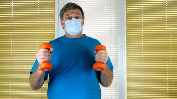 Mature Adult Man with Dumbbells in Hand Runs on Spot at Home Near Window with Blinds alt