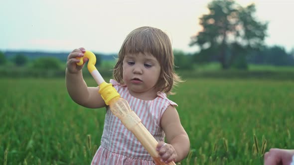 A Little Girl Tries to Blow Soap Bubbles in Nature alt