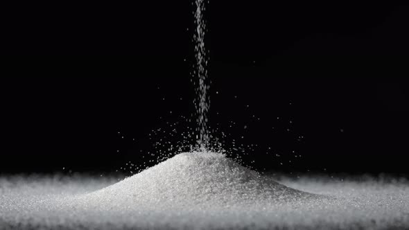 Particles of White Dry Sand are Pouring Down Forming Hill on an Isolated Black Background alt