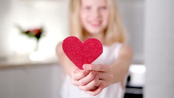 Red Heart Close Up in Hands of Little Blonde Smiling Girl on Valentines Day alt