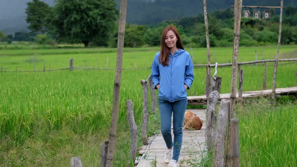 A beautiful young asian woman walking across bamboo bridge in paddy field