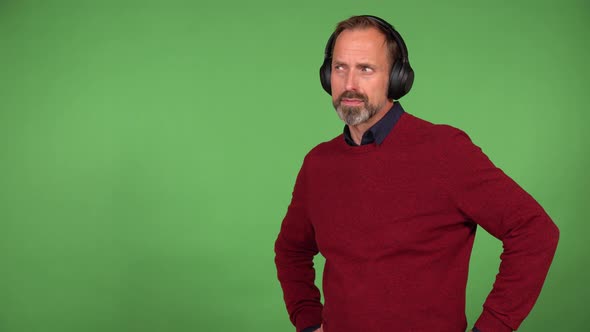 A Middleaged Handsome Caucasian Man Listens Something with Headphones on  Green Screen Background