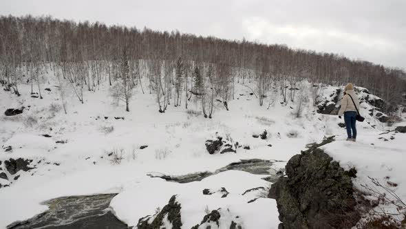A Tourist Girl Stands on Top of a Hill in the Mountains in the Winter Forest alt