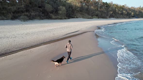 A guy in a tracksuit runs along the beach with his dog at sunrise. Motivation, training, friendship