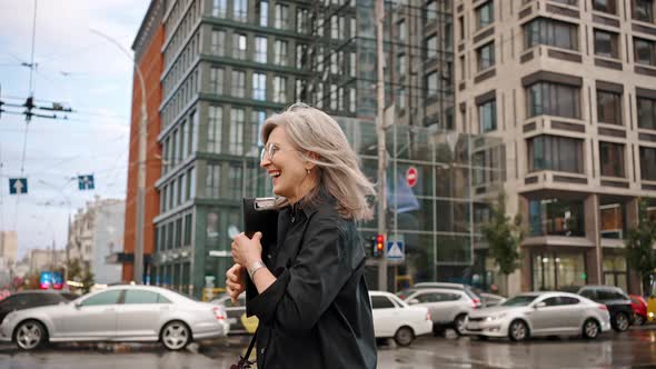 Beautiful Urban Mature Woman Running Down the Street in the Rain Without an Umbrella Hiding Behind a alt