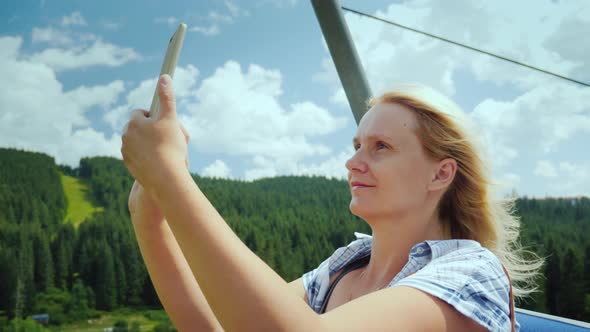 An Active Woman in the Cabin of a Ski Lift Photographs Beautiful Views of Mountains and Forests alt