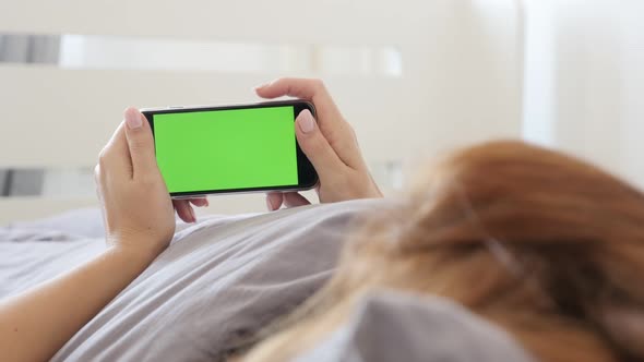 Female relaxing in bed while holds green screen gadget 4K 2160p 30fps UltraHD footage - Greenscreen  alt