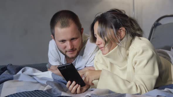 Married couple lies in bed using smartphones. Couple Of spouses lying on bed And watching
