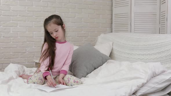 Cute Little Girl Drawing Pictures While Lying on Bed