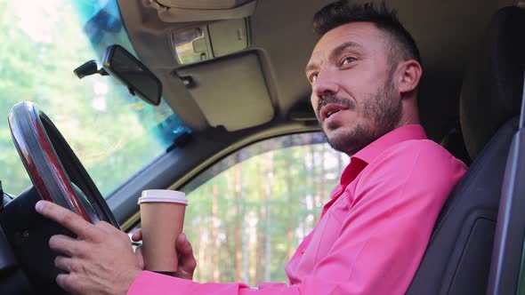 Happy Businessman Sits Behind the Wheel Drinks Coffee Smiles and Talks alt
