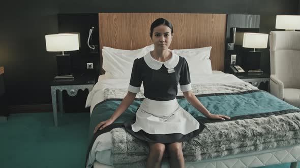 Housekeeper Sitting on Bed in Luxury Hotel Room alt