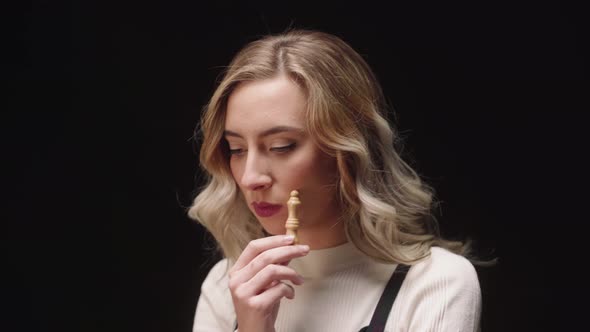 Caucasian Woman Holding Bishop Chess Piece, Touching Face While Thinking Of Strategy. close up alt