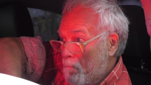 Drunk Aged Man with Beard and Glasses Sits in Automobile alt