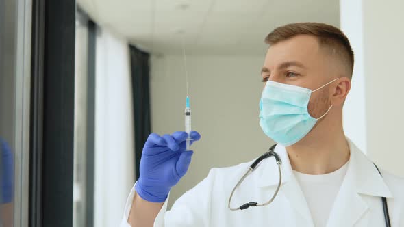 Young Doctor in a Protective Mask with a Vaccine Syringe in His Hands alt