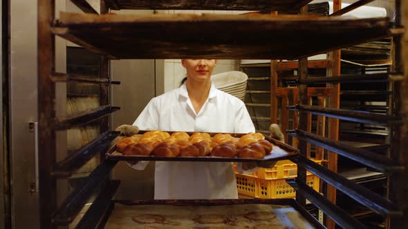 Female baker putting baked michetta in baking trolley alt