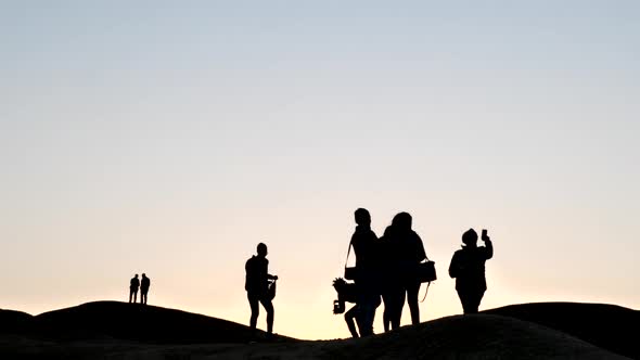 Wide shot of people in silhouette against a pink sky in the Namib desert at sunset alt