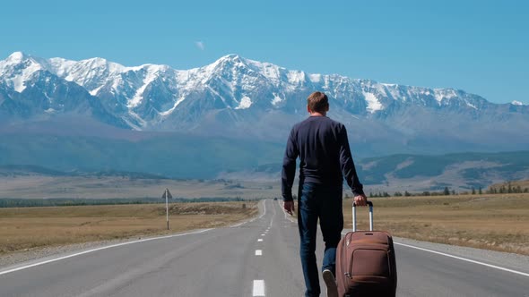 Man Traveling with Suitcase on a Mountain Road alt