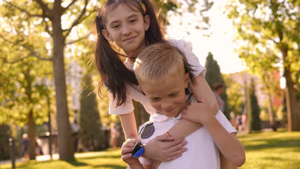 A Little Girl Hugs a Boy From the Back in the Park in Summer alt