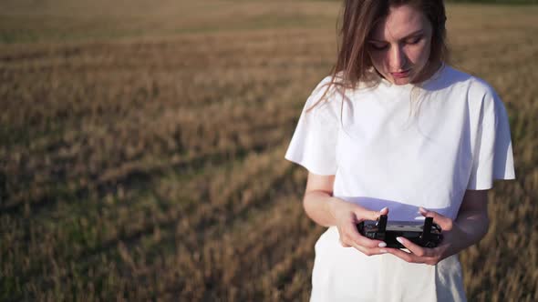 A Beautiful Young Woman in a Field Controls a Drone in Flight. Control the Drone Through a Remote