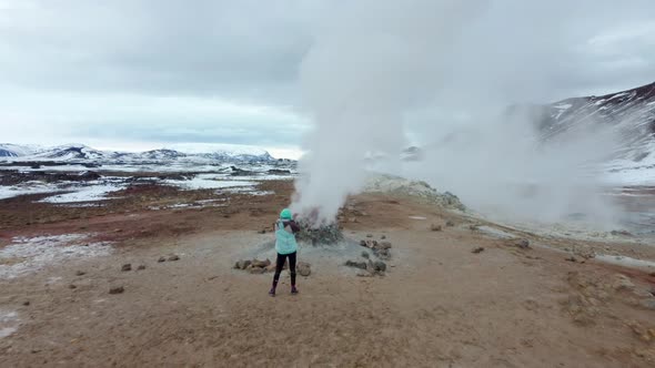 Woman watching geothermal field with fumaroles and geysers. Area with natural steam vents and mud po alt