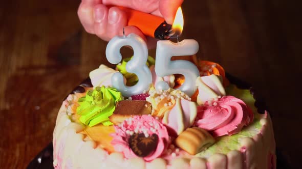 Hand lights the candles on the cake. 35th birthday. Birthday cake with a burning birthday candle alt