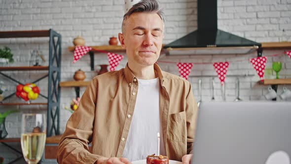 Happy Middle Aged Birthday Man Making Wish and Blowing Candle on Cupcake Video Chatting with Family alt