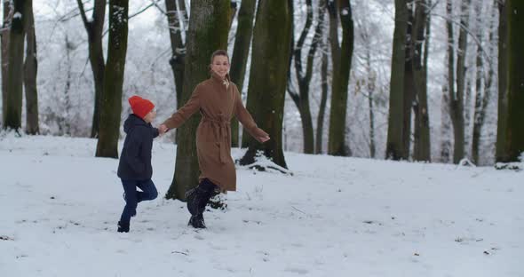 Mom With A Small Child Playing In A Snowy Park alt