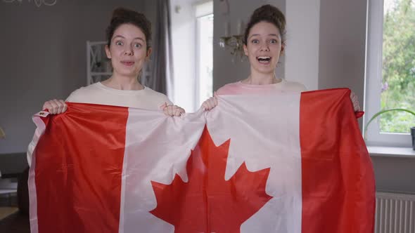 Excited Twin Sisters Hockey Fans with Canadian Flag Supporting TV Match in Living Room at Home alt