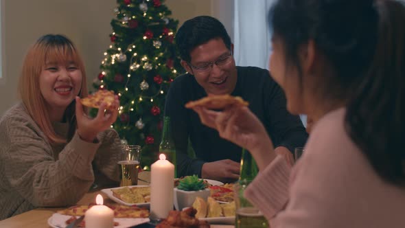 Asian family party with beer and pizza food near christmas tree at house in night.