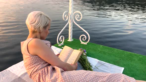Beautiful Girl on a Raft on the Lake Sits on a Blanket and Reads a Book