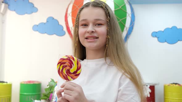 Close Up Portrait of Beautiful Cute Baby in White Tshirt Holding Lollipop and Looking at Camera alt