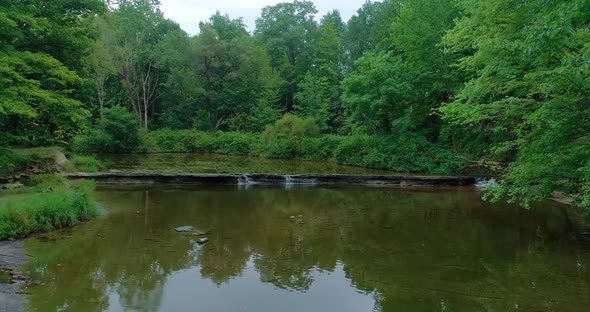 Aerial shot of five small waterfalls trickling into a creek that is flowing through a forest. alt