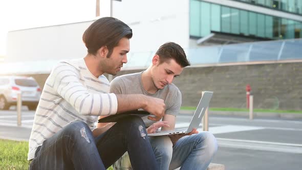 two young multiethnic men sitting outdoor using digital tablet and personal computer alt